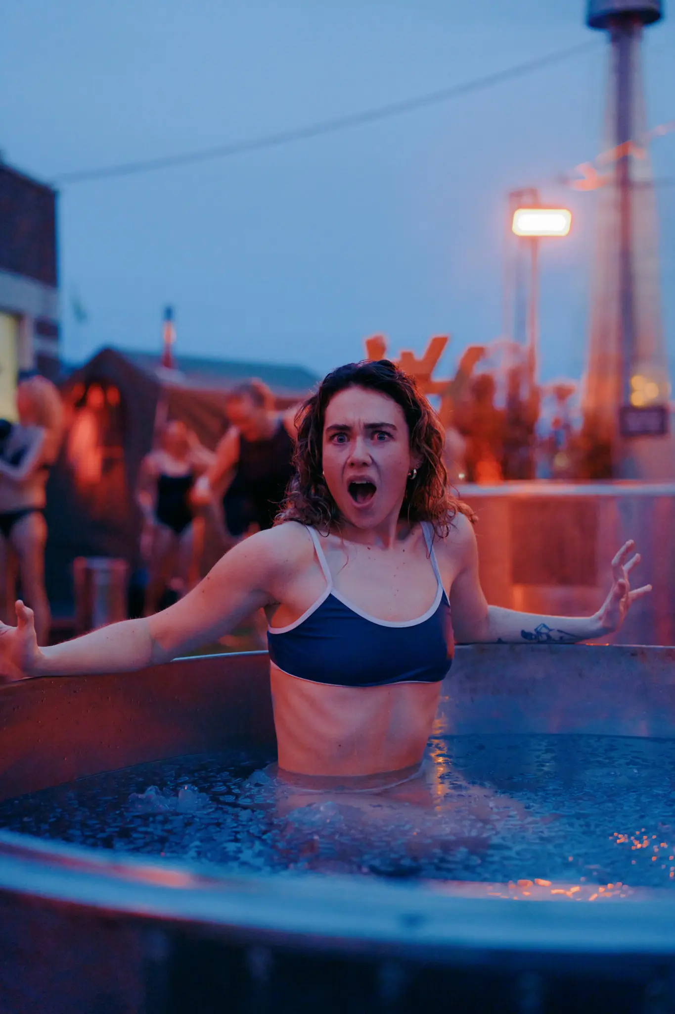 Woman in blue swimwear stands in waist-high water, with her mouth open in an excited expression. 