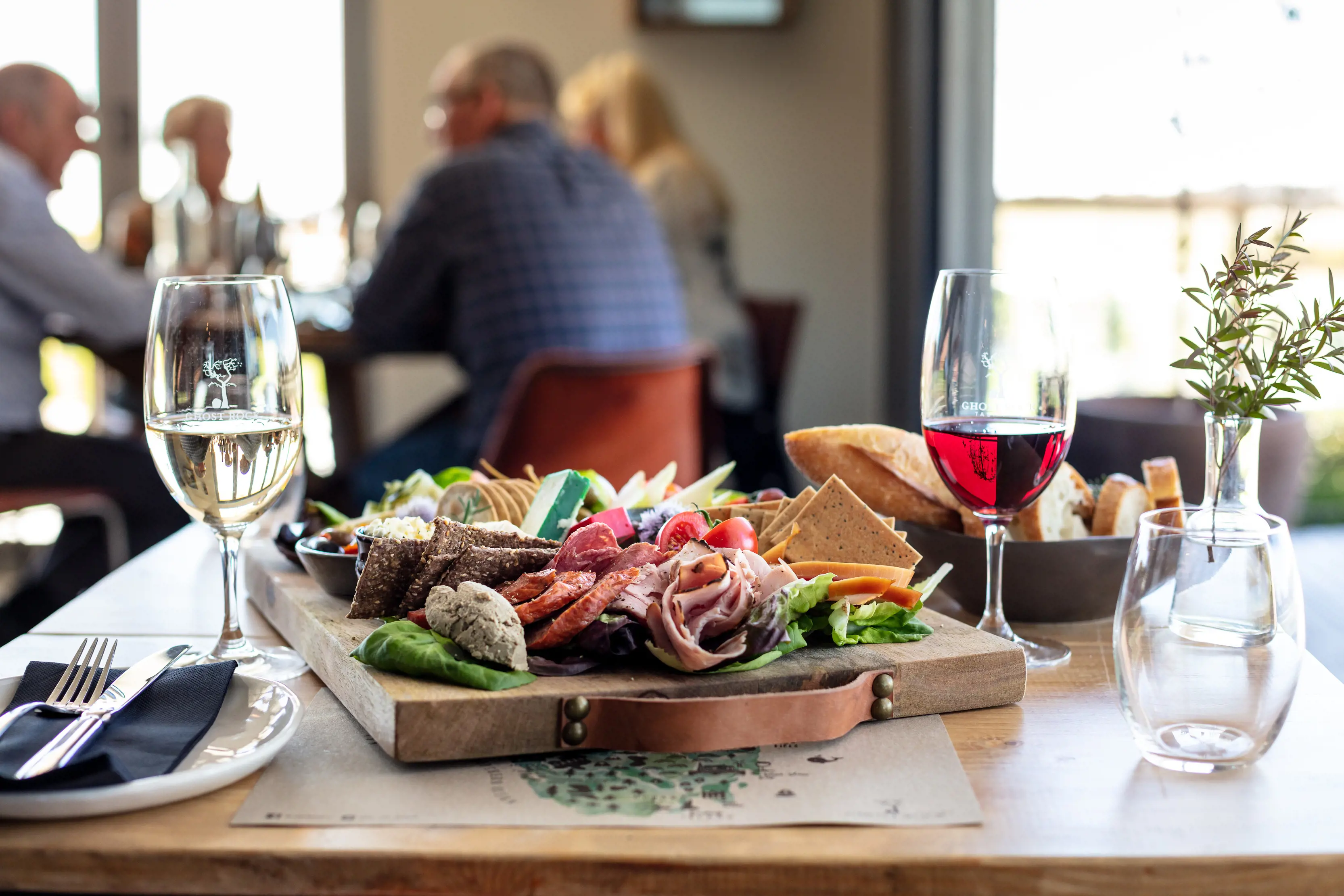 A platter of a variety of fresh food accompanied with a bowl of bread and a glass each of red and white wine.