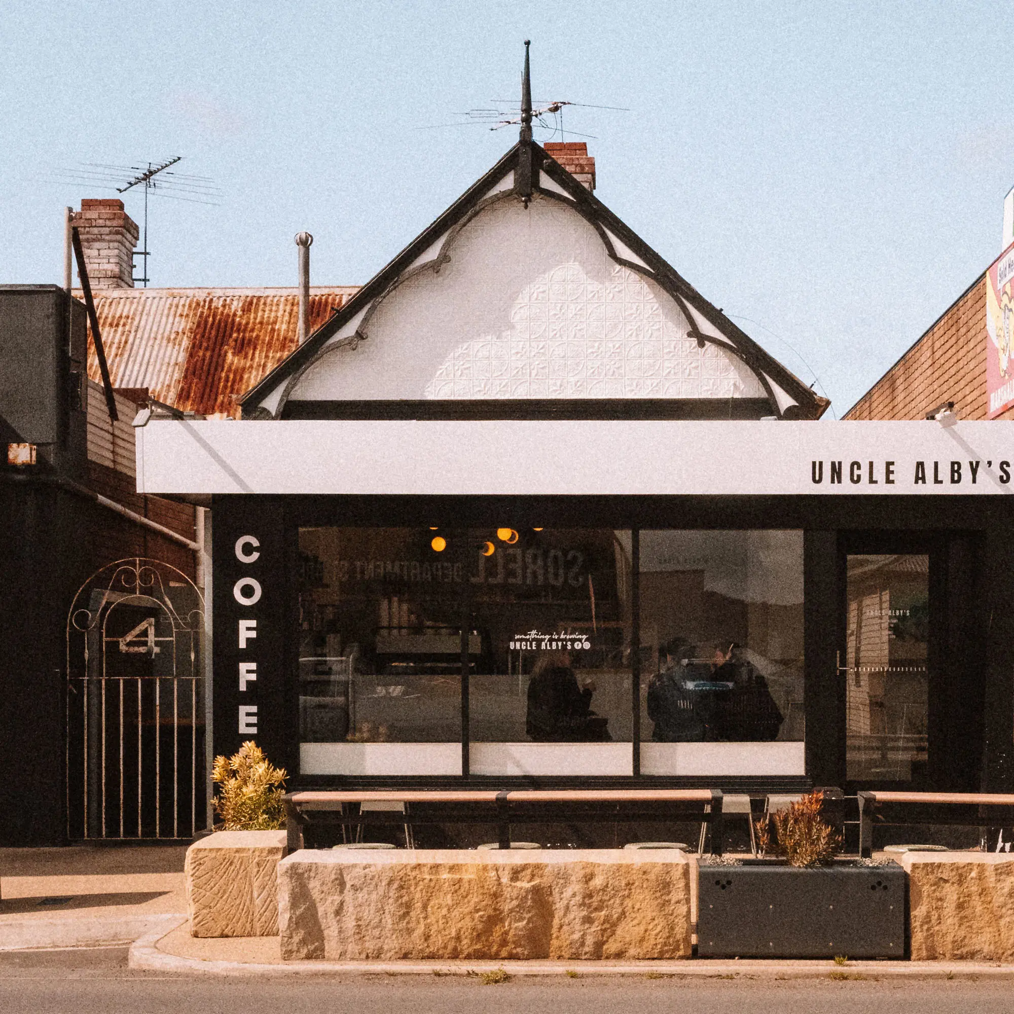 A black-painted shop building with a distinctive peaked roofline, and signage saying "Uncle Alby's" and "coffee"..