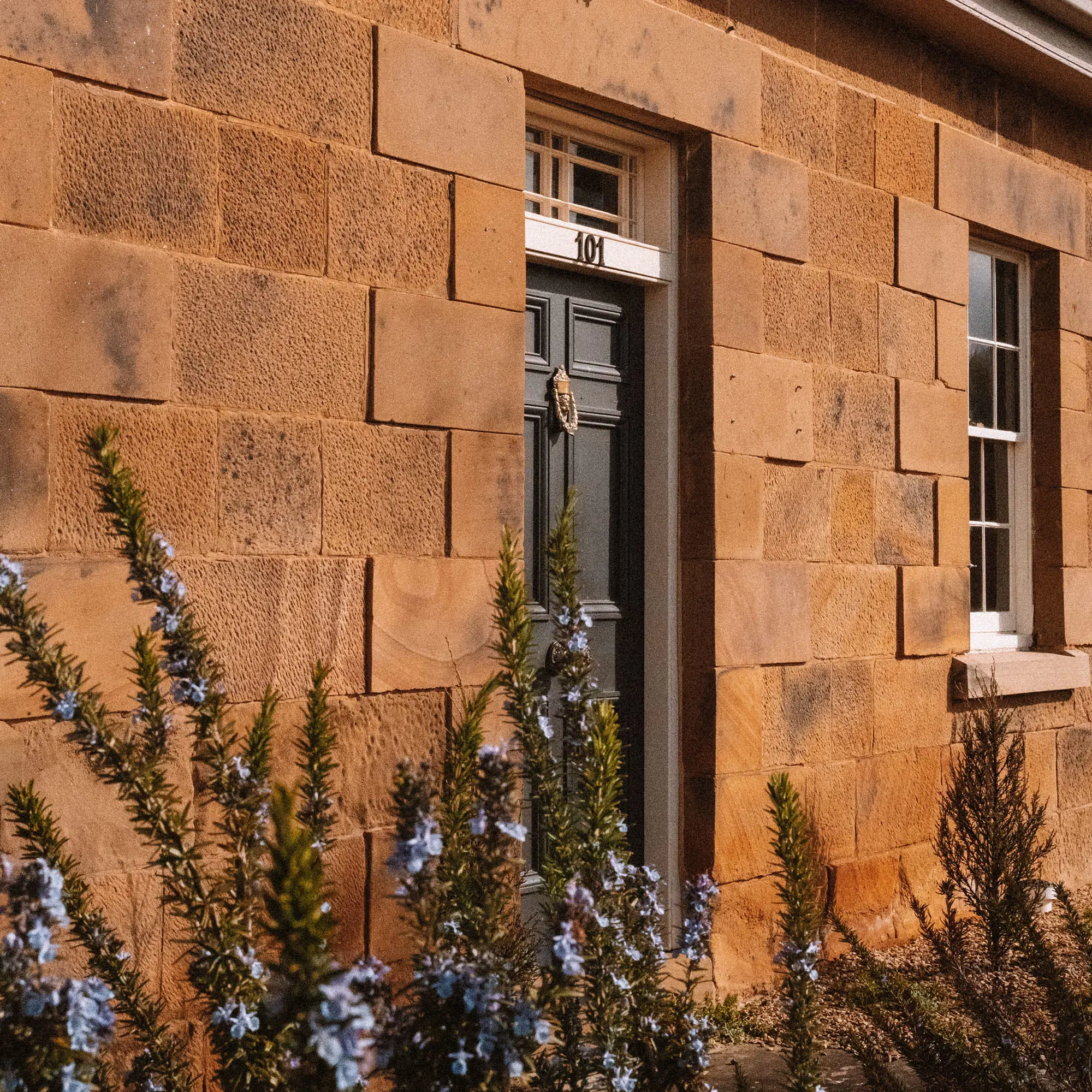 The front of a standstone-built Georgian cottage, with a dark door, gold door-knocker and the numbers '101' on the lintel.