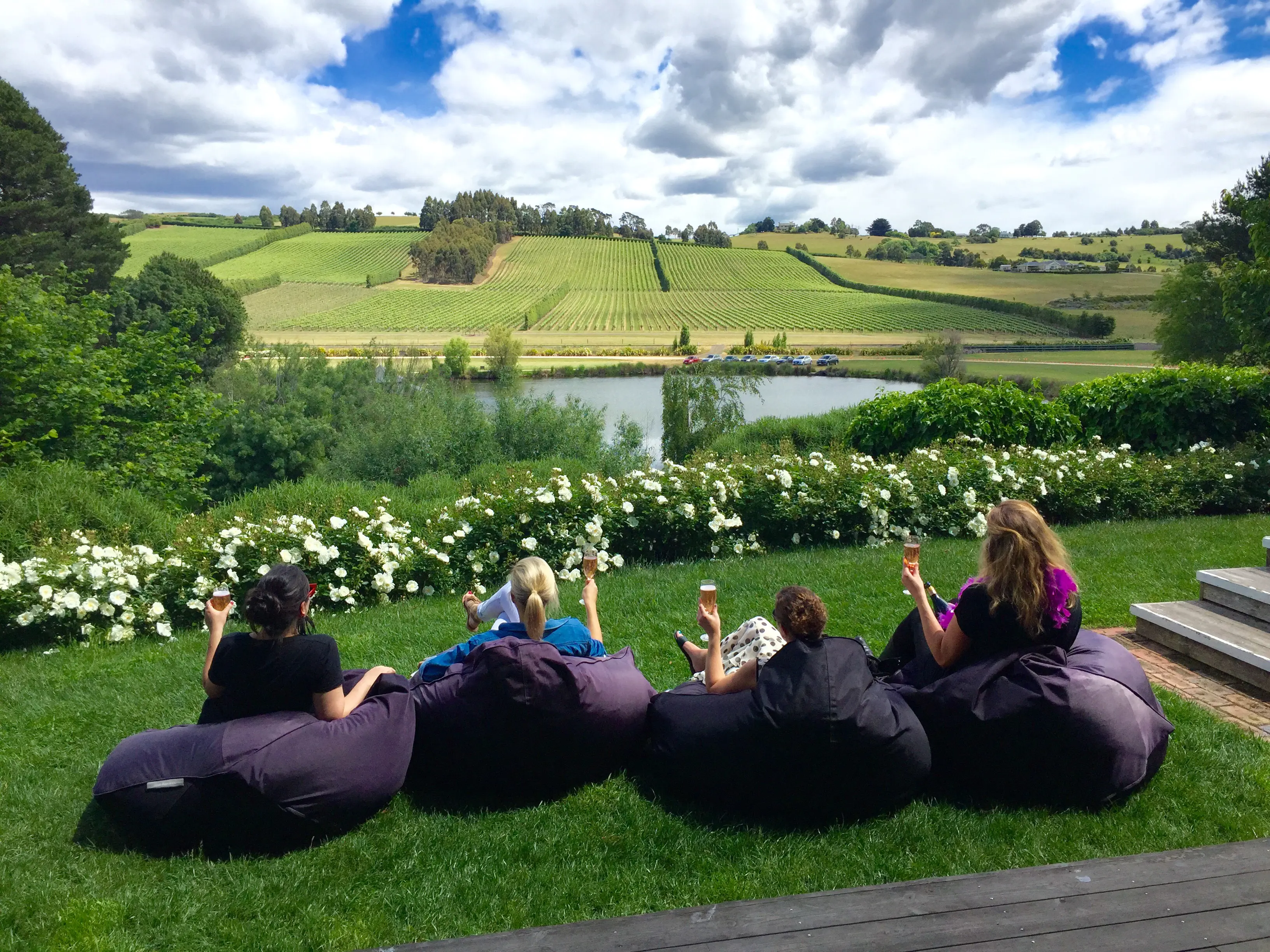 Four ladies enjoy a glass of wine while sitting in comfy bean bags at a winery, looking out to the lush greenery.