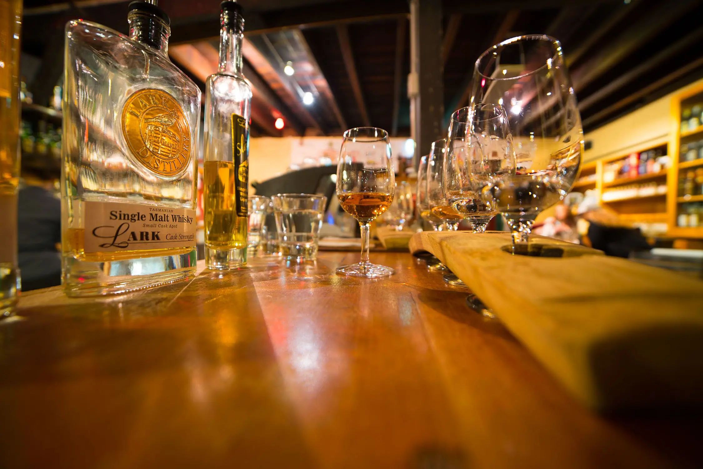 A close up of a whisky tasting at a wooden table, half-full bottles and whisky glasses dotted around.