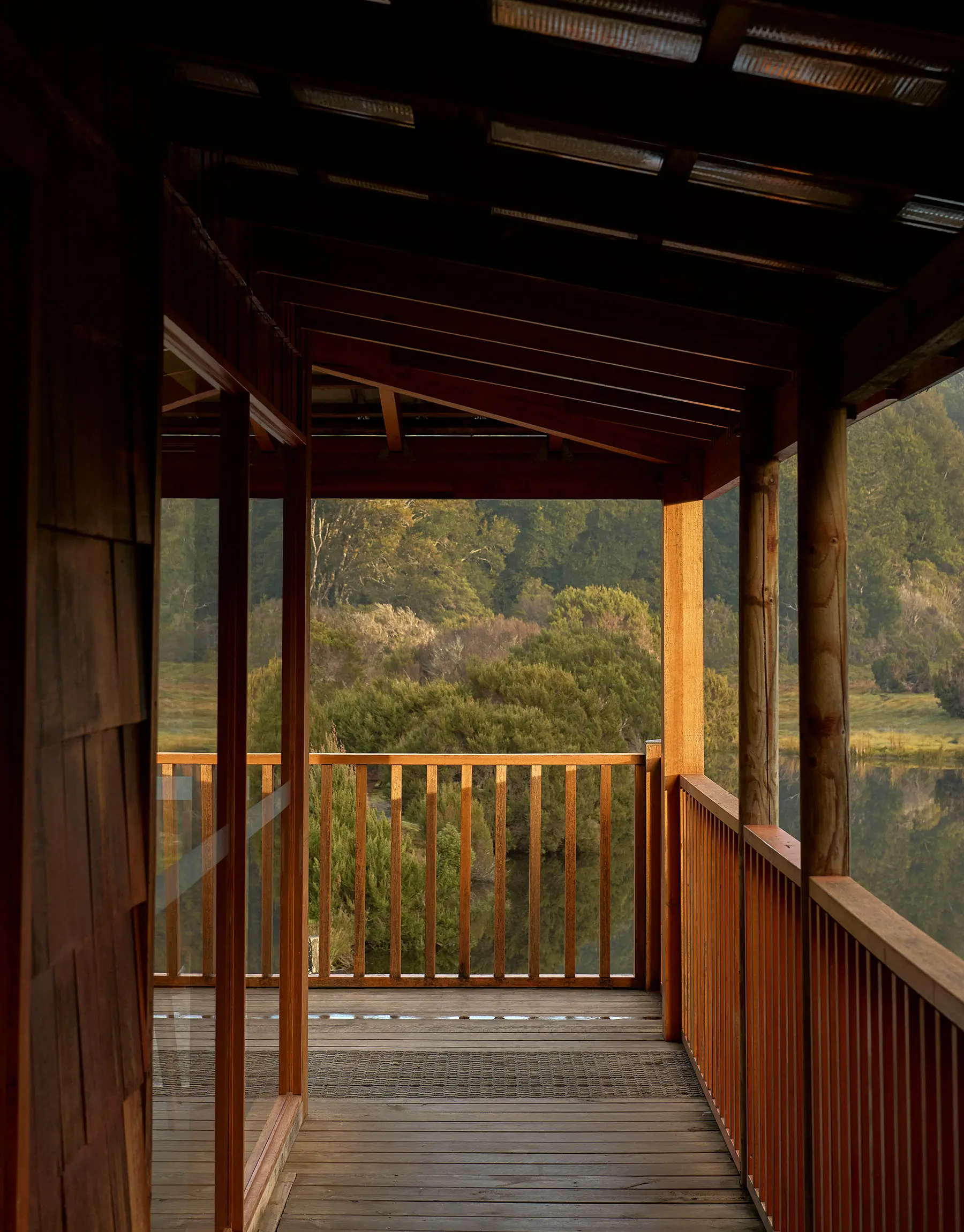 On a wooden wraparound deck, looking past the structure, which frames a view of native bush-covered mountains.