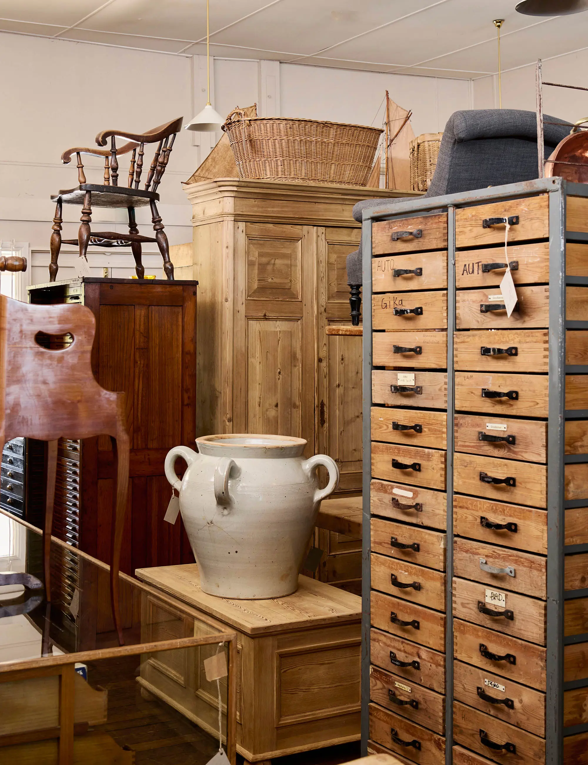 The interior of a vintage and antique store, featuring dressers, wardrobes and chests of drawers arranged neatly with brown paper price tags hanging off them.