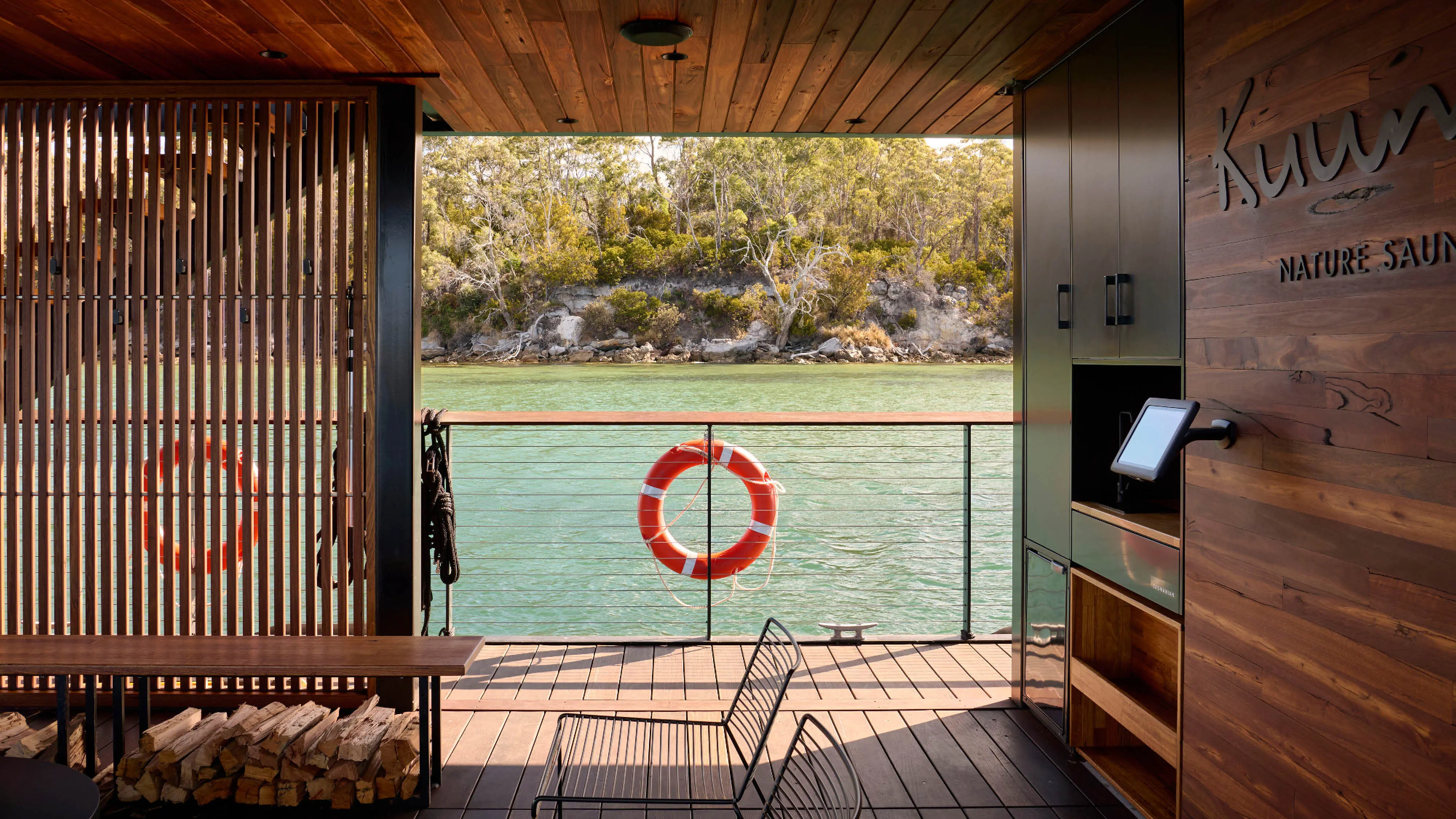 On board a floating sauna pontoon, artfully clad with wooden decking and walls. Over the railing are still river waters.