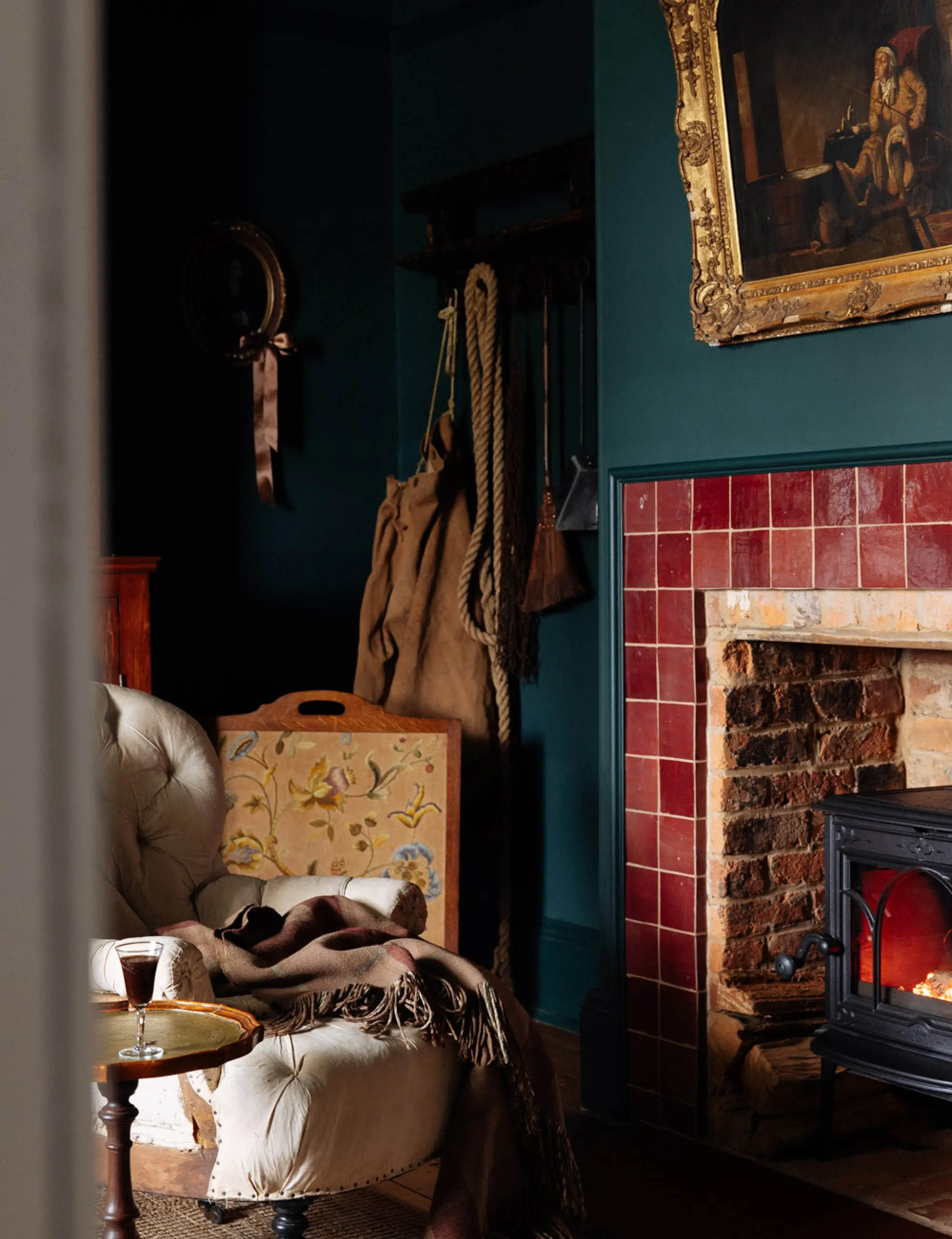 The interior of a cosy heritage sitting room, with a roaring fireplace, plush cream chairs and plenty of blankets and throws.