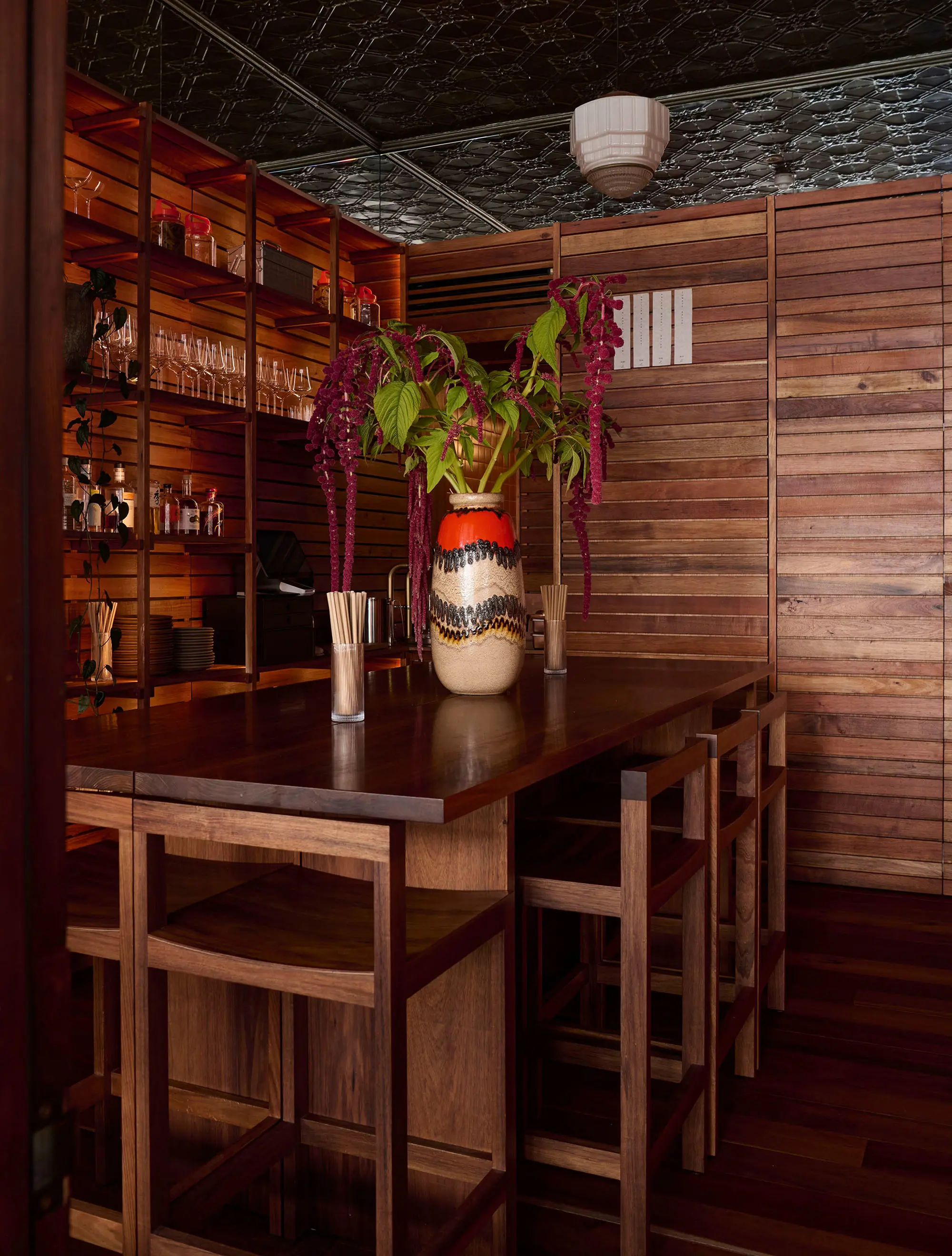 A dark and moody table in the corner of a Japanese-style bar. Glasses and bottles line shelves on the wall.