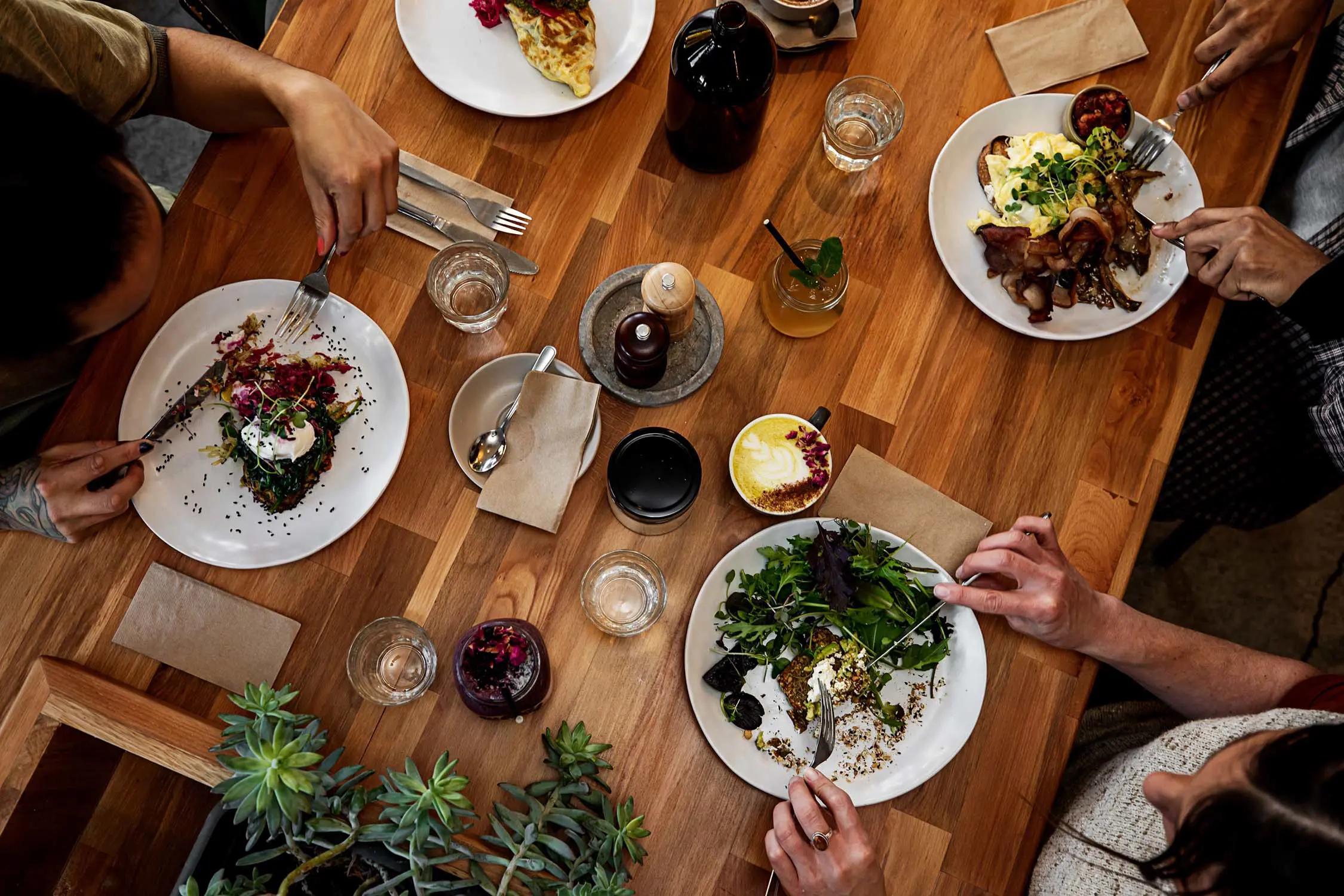 A top-down view of four people sitting around a table at a cafe, eating delicious meals and drinking coffee.