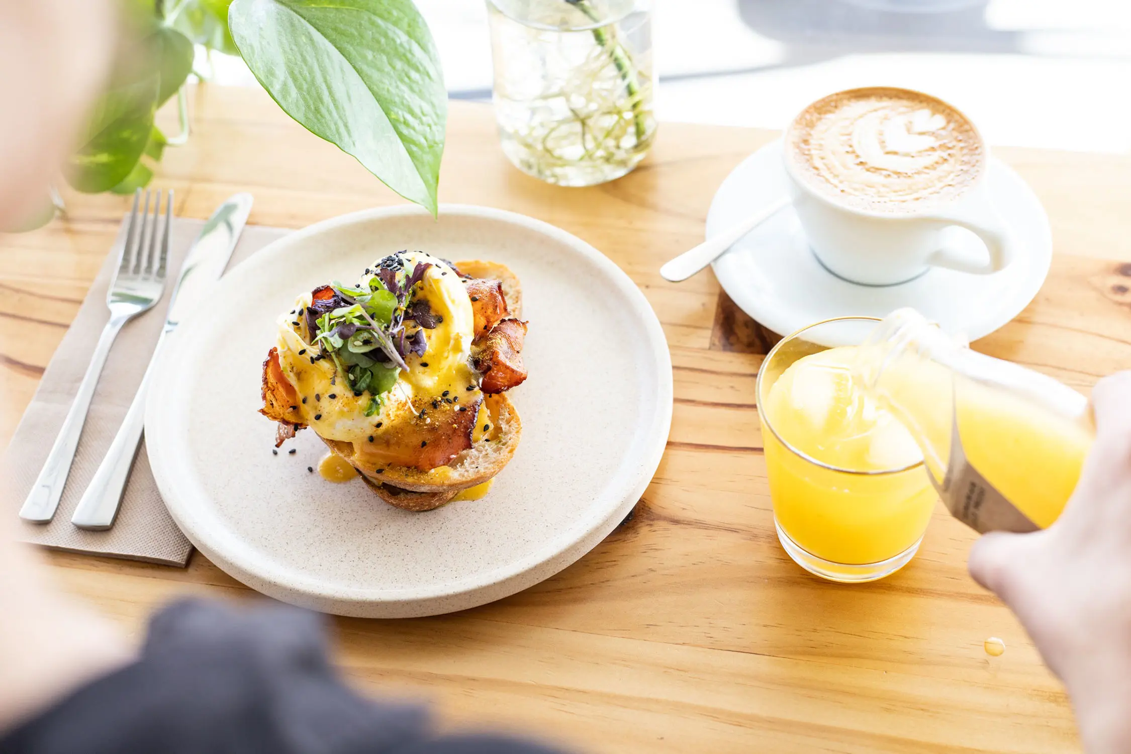 A delicious brunch meal, with a coffee and orange juice being poured into a glass, on a light wooden table.