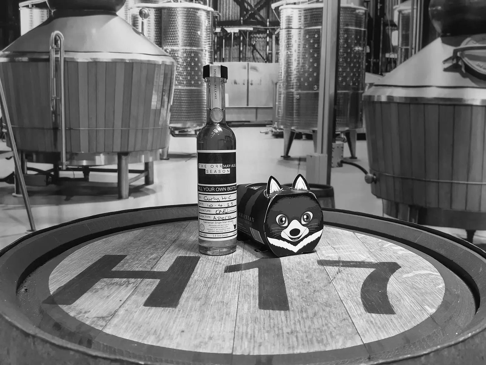 On top of a large wooden barrel sit a bottle of whisky and a cardboard gift box shaped as a tasmanian devil.
