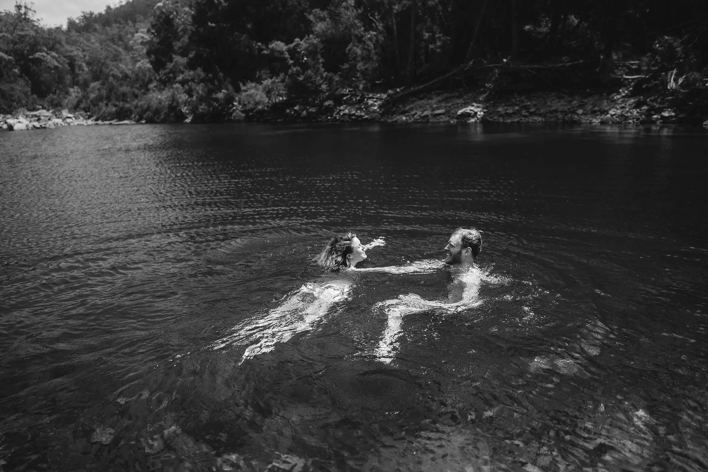 Two swimmers in the dark waters of a lake. The thick bush surrounds the banks of the watering hole.