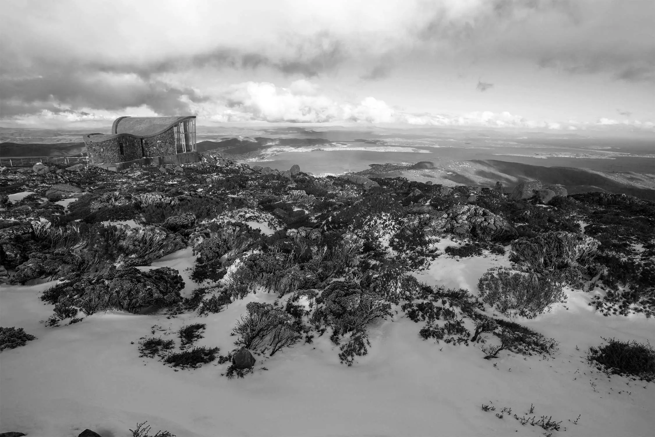 A rocky, snow-covered landscape showcases a scenic building at a high elevation under a cloudy sky.