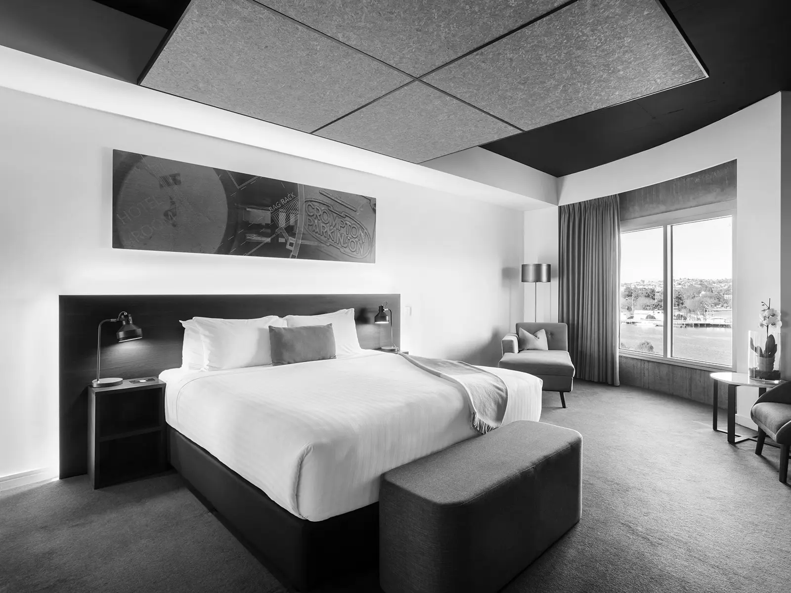 The interior of a sleek hotel room, featuring a large bed and soft furnishings.