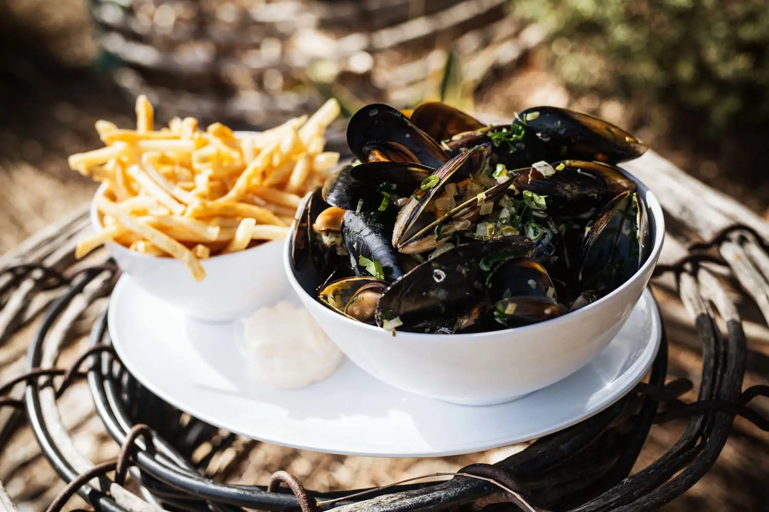 A plate with fresh shellfish ready to be eaten and a side of french fries, sitting on top of a wicker oyster cage.